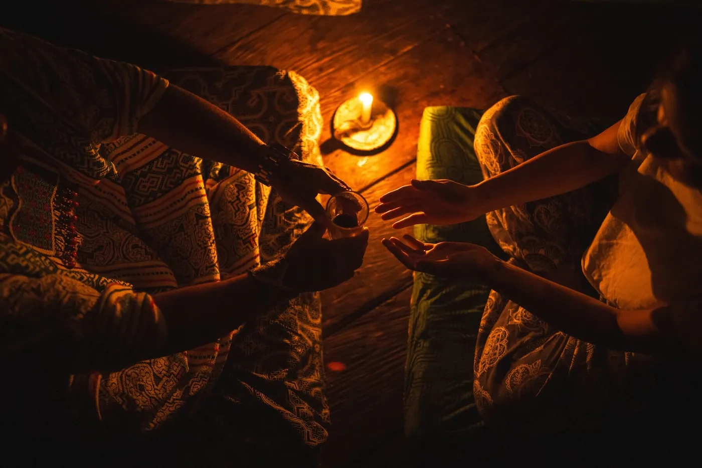 A cup of ayahuasca passed between hands by candlelight